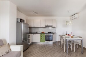 A modern kitchen with a built-in oven, a microwave, and a refrigerator. There is a dining table with chairs and a small kitchen island with a sink. - Wabi Sabi Apt2 Pool & Garden, Brzac, Croatia (Brzac)