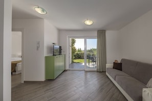 Ein modernes Wohnzimmer mit einer Couch, einem Fernseher und einer Schiebetür zu einem Außenbereich.