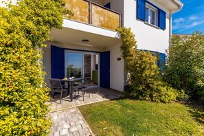Ein zweistöckiges Gebäude mit einem Balkon, einem Essbereich mit Stühlen und einem Tisch sowie einem gepflegten Garten.