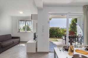 Ein modernes Wohnzimmer mit einer Couch, einem Fernseher und einem Essbereich mit Tisch, gedeckt für zwei Personen, einer Weinflasche und einem Baguette.