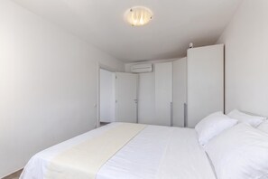 Une chambre à coucher comprenant un lit, une armoire, un appareil de climatisation et une porte donnant sur une autre pièce.