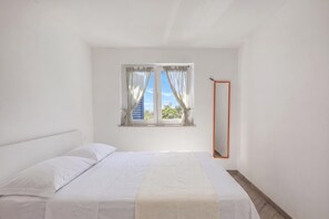 Ein Schlafzimmer mit einem Einzelbett, einem Fenster mit Vorhängen und einem Spiegel an der Wand.