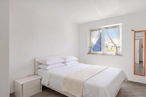 Une chambre à coucher avec un lit, une table de chevet, une fenêtre avec des rideaux et un miroir avec un cadre orange.