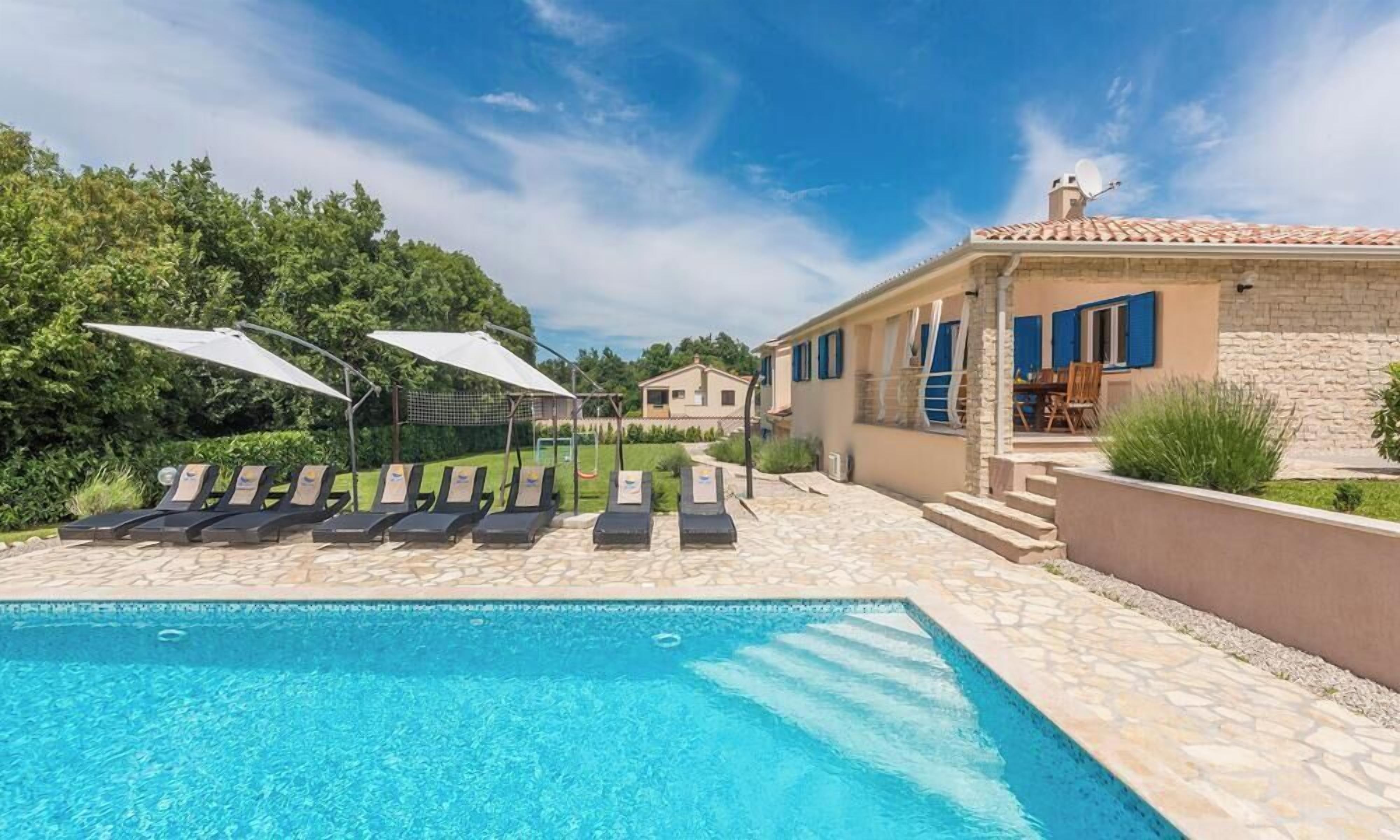 A swimming pool with lounge chairs, a covered area with umbrellas, and a building with a stone facade.