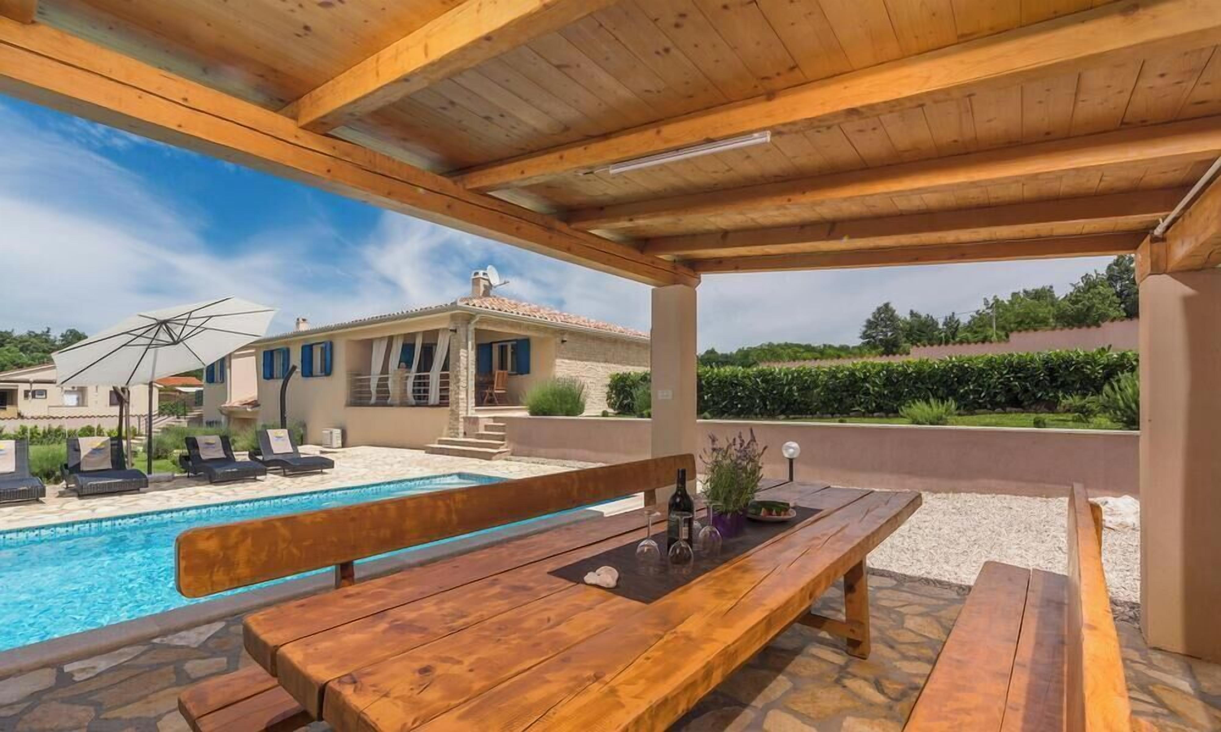 A wooden deck with a pool, lounge chairs, and a wooden table with bottles.
