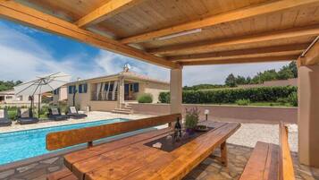 A wooden deck with a pool, lounge chairs, and a wooden table with bottles.