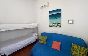 A room with bunk beds, a blue sofa with patterned cushions, a painting of a tree and rocks, and an air conditioning unit. - Nice home in Costa Rei with WiFi (Costa Rei)