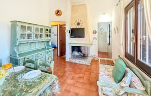 A dining area with a table set for two, a fireplace, and a television mounted above it. - Nice home in Costa Rei with WiFi (Costa Rei)