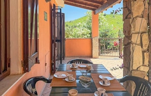 An outdoor dining area with a table set for four, a wooden pergola, and a view of a hillside. - Nice home in Costa Rei with WiFi (Costa Rei)