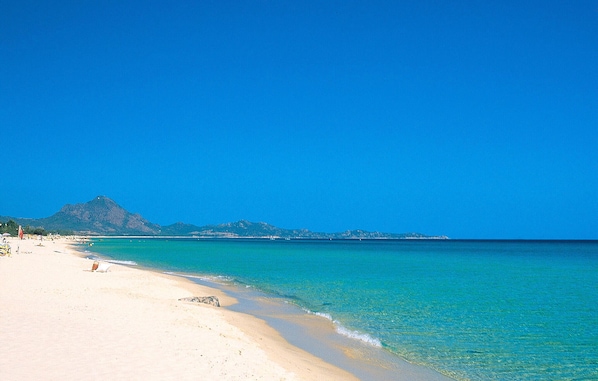 A beach with clear turquoise water, a sandy shore, and a mountain in the background. - Nice home in Costa Rei with WiFi (Costa Rei)