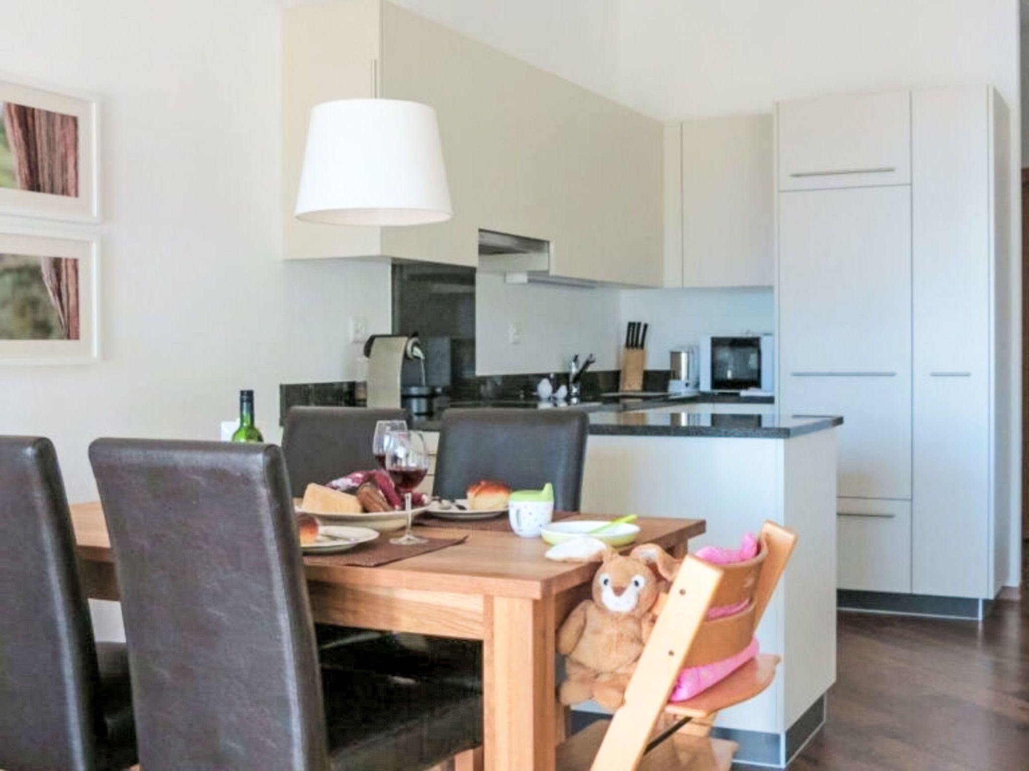 Una cocina moderna con armarios blancos, una mesa de comedor con sillas y un peluche en una de las sillas.