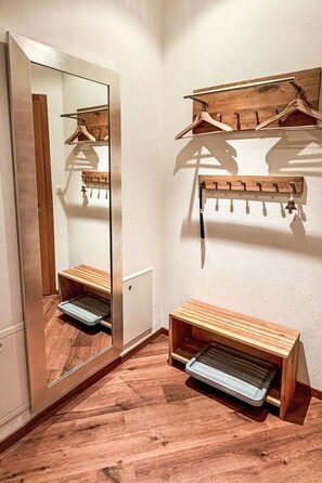 Ein Flur mit einer Holzbank, einem Spiegel und Holzkleiderhaken.