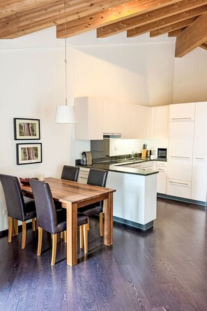 Eine moderne Küche mit weißen Schränken, einem Holzespeisetisch mit Stühlen und einer Pendelleuchte.