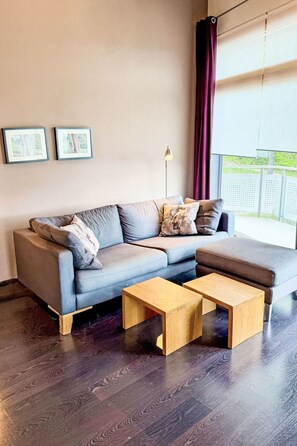 Ein modernes Wohnzimmer mit einem grauen Ecksofa, zwei Holztischen und einer Stehlampe.