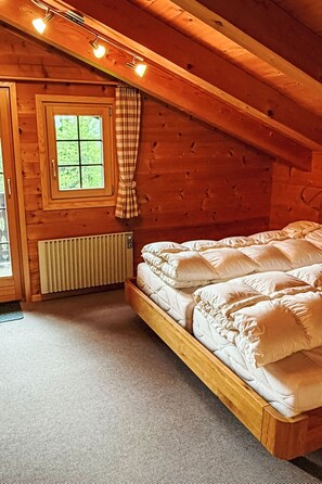 Un dormitori de cabana de fusta amb un llit, una finestra amb cortines i un radiador.