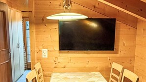 Ein Holzinterieur mit einem Esstisch, Stühlen, einem Flachbildfernseher und einer Deckenleuchte.