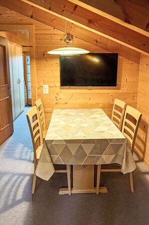 Ein Holzinterieur mit einem Esstisch, Stühlen, einem Flachbildfernseher und einer Deckenleuchte.