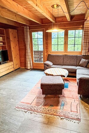 A wooden cabin interior with a sofa, ottoman, and a television on a wooden cabinet. - Zum Hirsch - upper floor by Interhome (Bellwald)