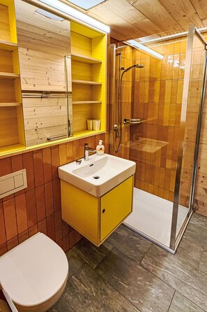 A bathroom with a yellow vanity, a white sink, a toilet, and a glass-enclosed shower. - Zum Hirsch - upper floor by Interhome (Bellwald)