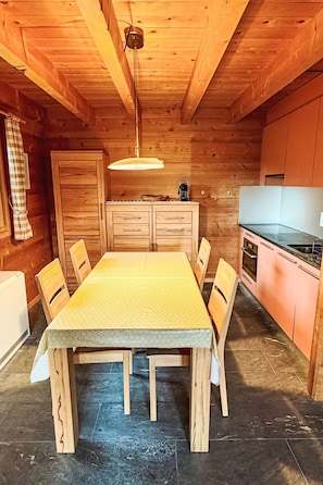 A wooden interior with a dining table, chairs, a kitchen area, and a ceiling light fixture.
