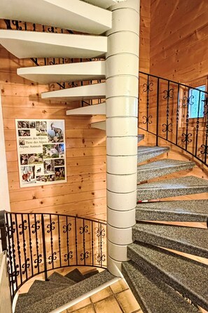 A spiral staircase with granite steps and a white central column, surrounded by wooden walls and a poster of alpine animals. - FeWo zum Hirsch - Erdgeschoss by Interhome (Bellwald)