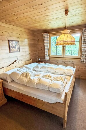 Quarto de cabana de madeira com uma cama, uma mesa de cabeceira, uma janela com cortinas e um abajur.