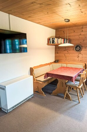 Um quarto acolhedor com teto de madeira, um sofá, uma mesa com toalha vermelha, uma estante e uma TV na parede.