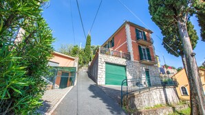 Edifici de dues plantes amb façana de pedra, porta de garatge verda i un balcó amb barana metàl·lica.