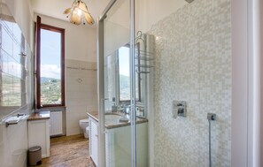 Et badeværelse med bruser, toilet og håndvask, et vindue med udsigt og en hængende lysarmatur.