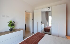 Ein Schlafzimmer mit Bett, Schminktisch, Spiegel und einer Topfpflanze.
