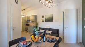 Eine moderne Küche mit Essbereich, inklusive Tisch gedeckt mit Obst und Wein, einer Couch und einer Pflanze.