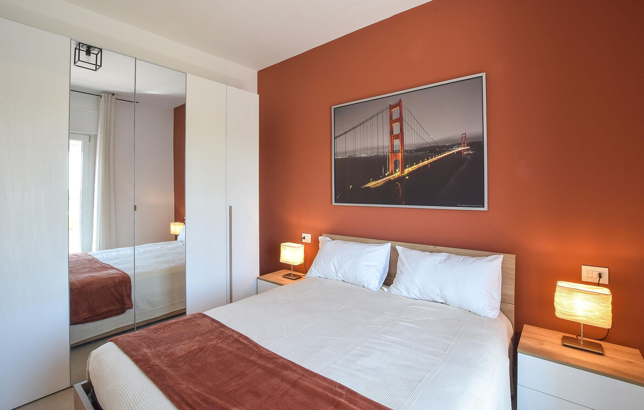 Une chambre d’hôtel avec un lit, une table de chevet, une lampe, un miroir et un tableau encadré représentant le Golden Gate Bridge.