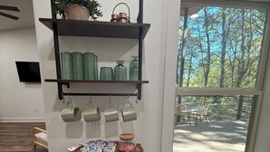 Un coin cuisine équipé d’un four à micro-ondes, d’étagères contenant des ustensiles de cuisine, d’une poubelle et d’une fenêtre donnant sur les arbres.
