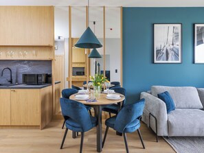 Een moderne keuken met houten kastjes, een zwarte magnetron, en een eethoek met blauwe stoelen en een ronde tafel.
