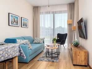 Un salon comprenant un canapé, une petite table, un fauteuil et un téléviseur fixé au mur.