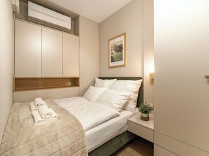 Een netjes opgemaakt bed met een gevouwen handdoek, een kamerplantje en een ingelijst beeld aan de muur.