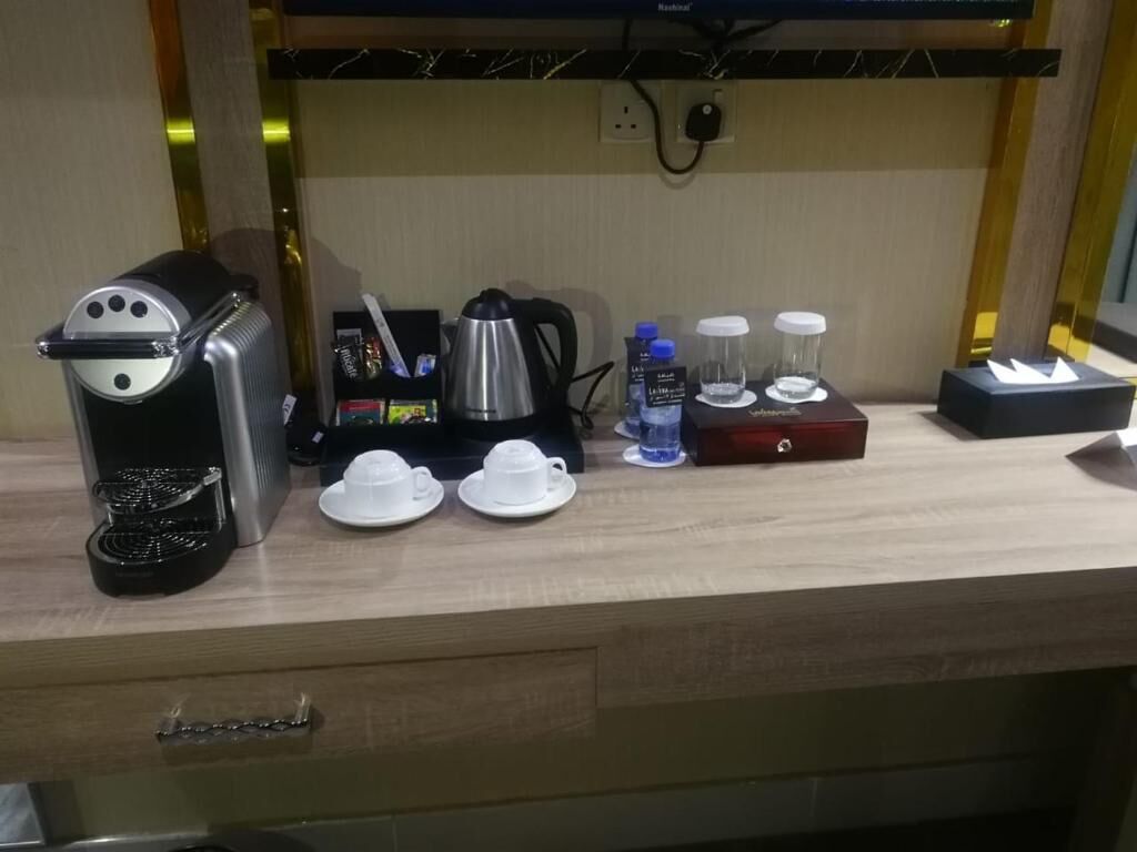 A kitchenette with a coffee maker, kettle, cups, and condiments.