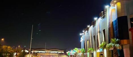 Un edificio moderno con fachada curva, iluminado por farolas, bajo un cielo despejado.