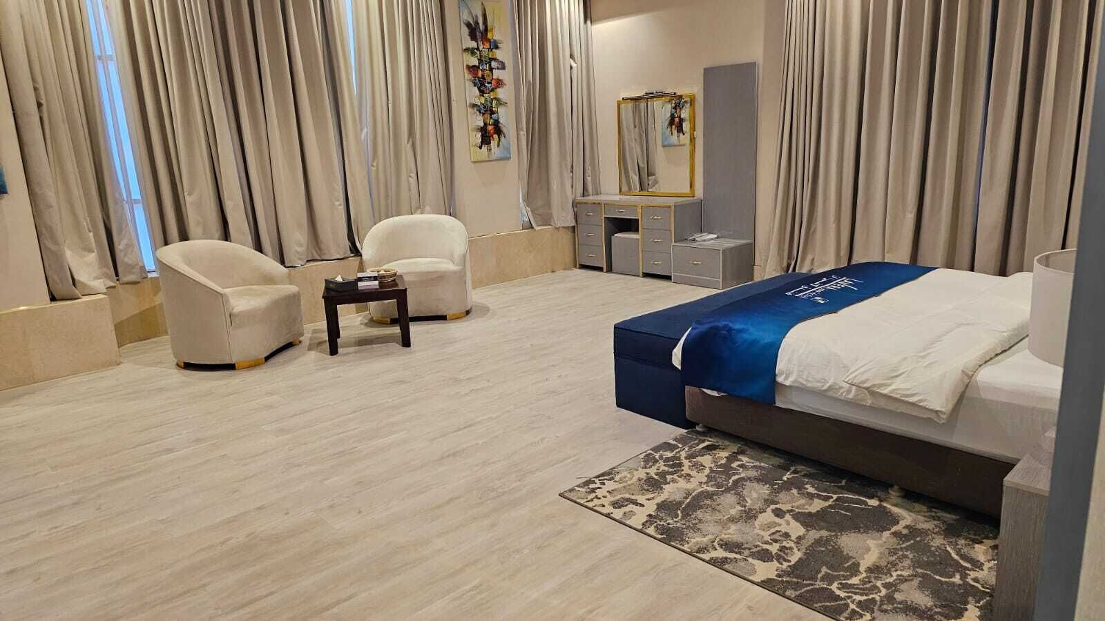 Een moderne hotelkamer met een bed, twee stoelen, een klein tafeltje, een spiegel en een decoratief object aan de muur.