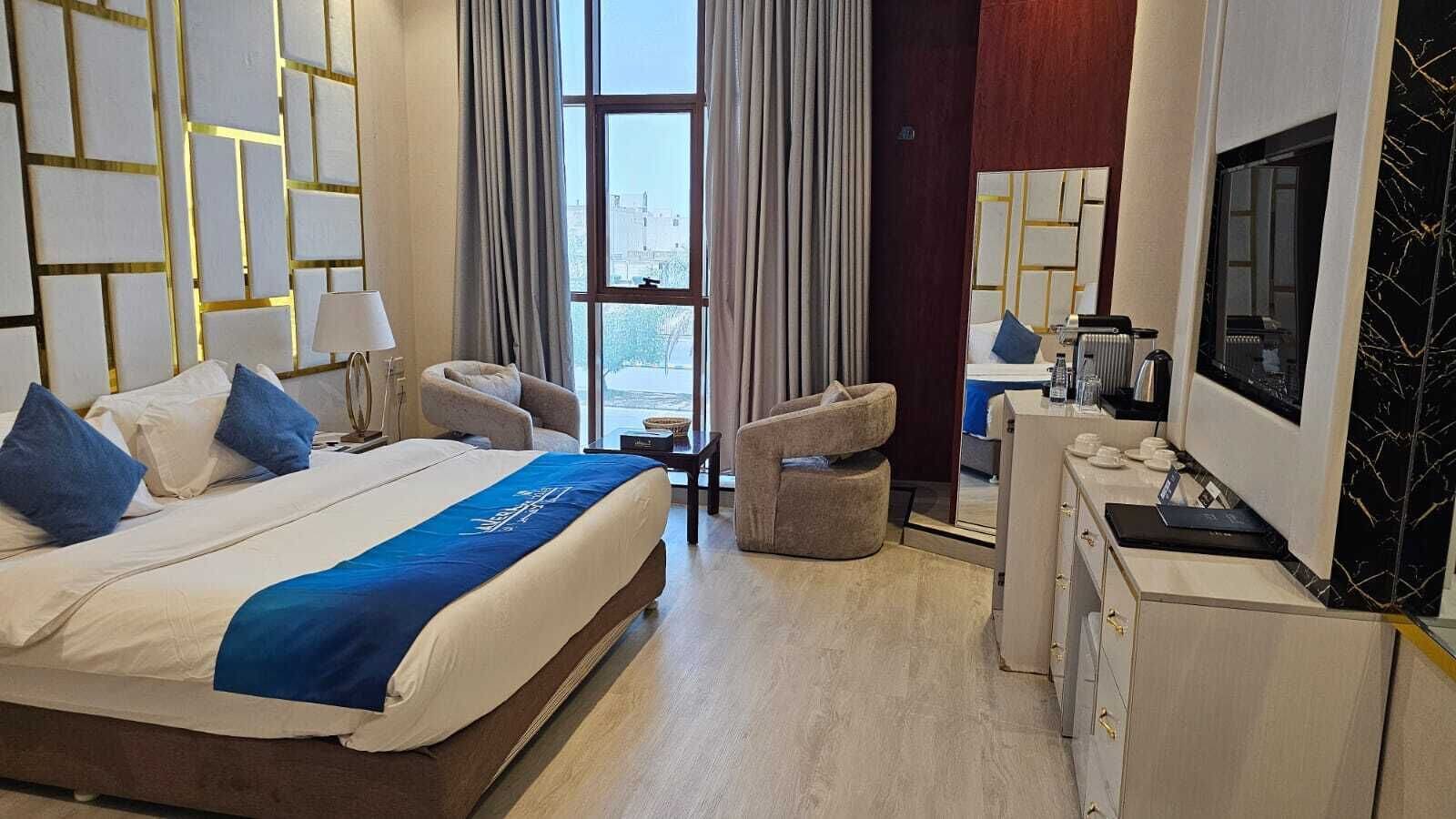 A hotel room with a bed, a desk, a chair, a TV, and a window with curtains.