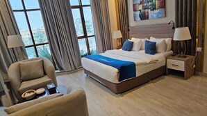 A hotel room with a large bed, two bedside tables, a chair, and a view through large windows. - Lavera inn Hotel (Riyadh)