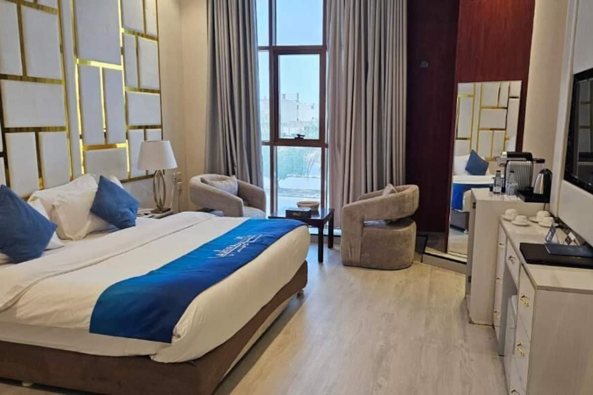 A hotel room with a bed, two armchairs, a desk with a TV, and a large window.