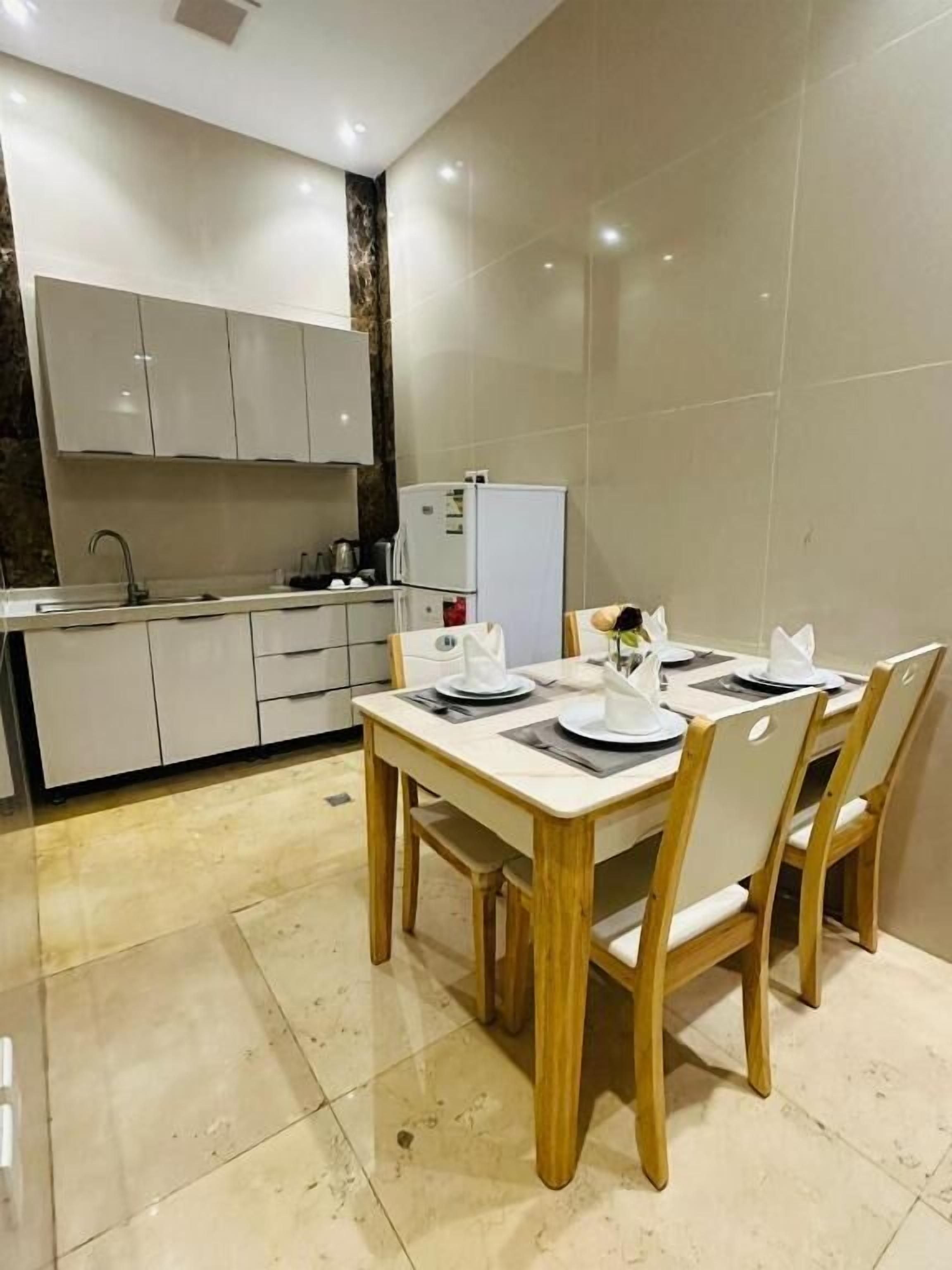 Una cocina moderna con armarios blancos, una mesa de comedor para cuatro personas y un refrigerador.