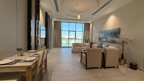 Een moderne woonkamer met een eethoek, grote ramen en een schilderij aan de wand.