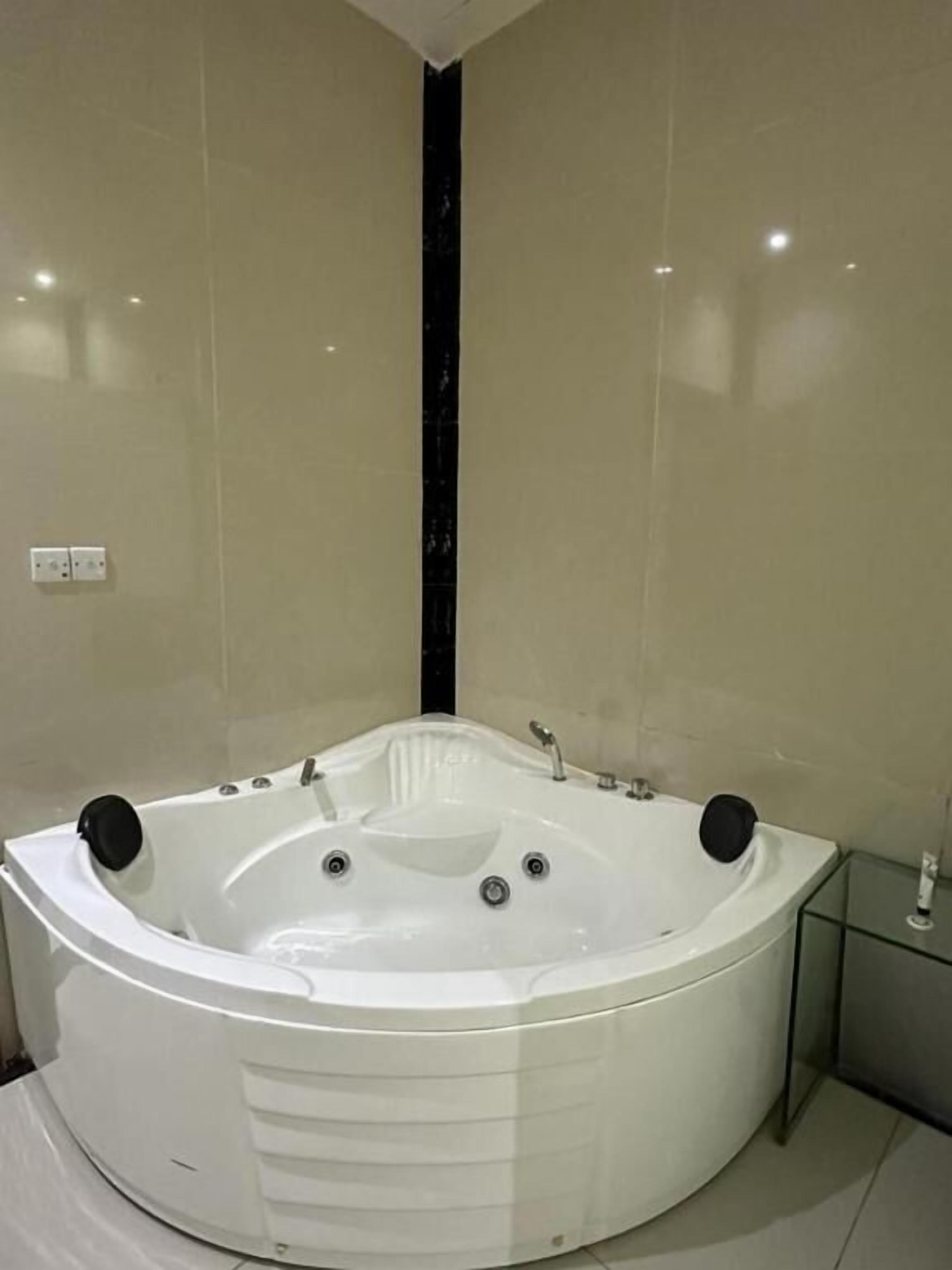 Eine große, runde, weiße Badewanne in einem modernen Badezimmer, mit einer Glasabtrennung und einem schwarzen, vertikalen Wandelement.