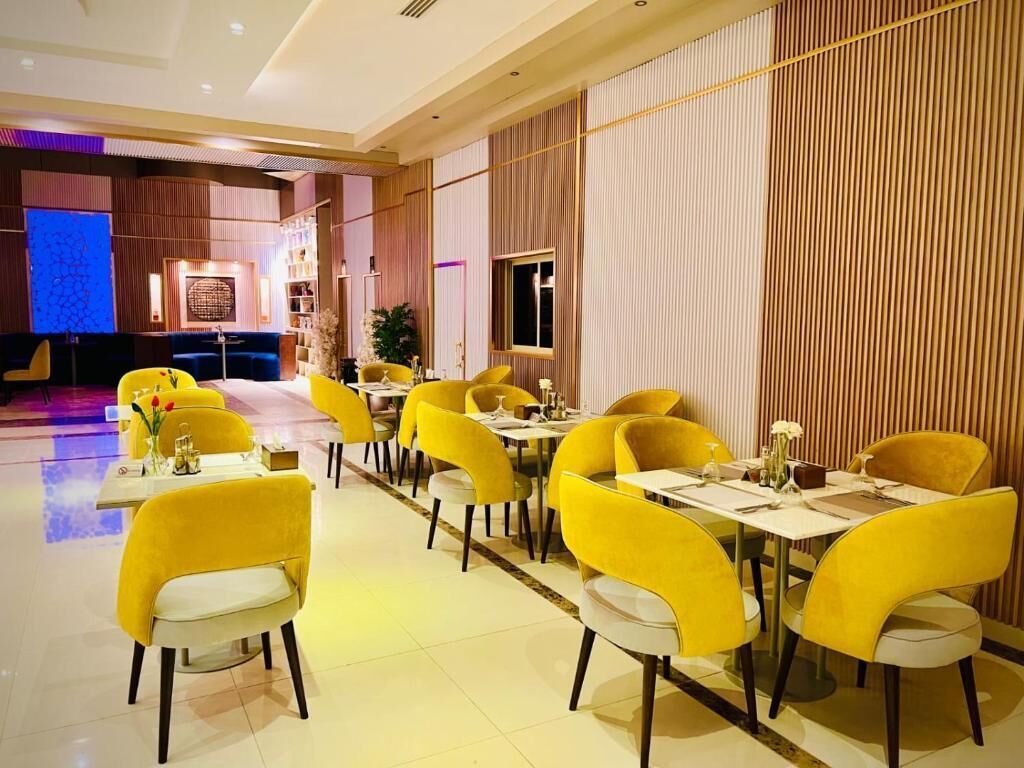 Restaurante com cadeiras e mesas amarelas, palco ao fundo e design de interiores moderno.