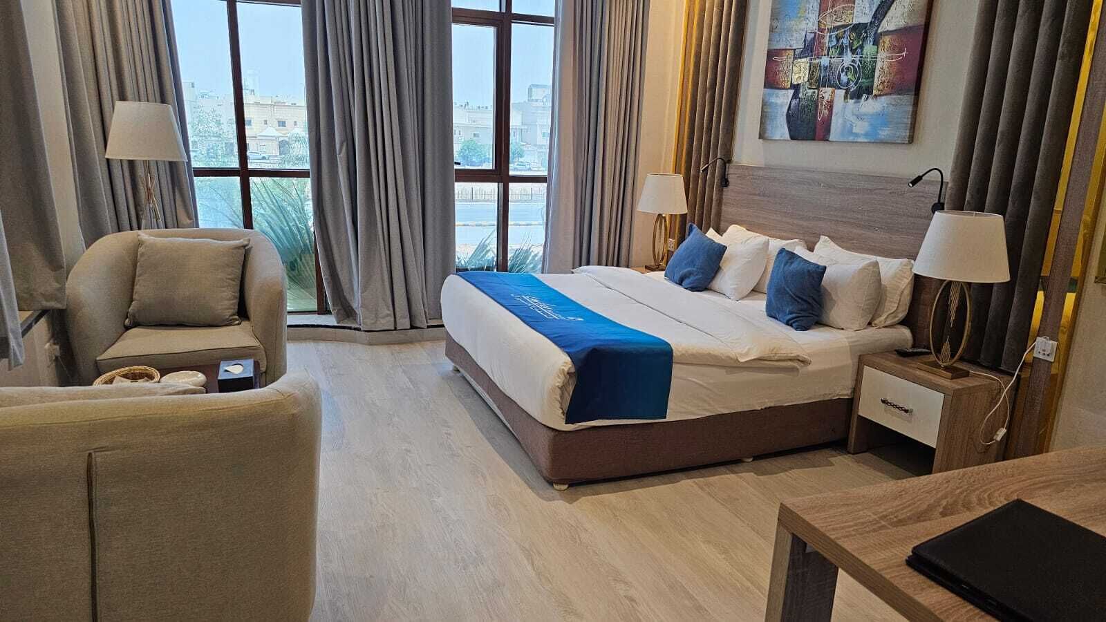 A hotel room with a large bed, a chair, a nightstand, and a view of the city through the window.