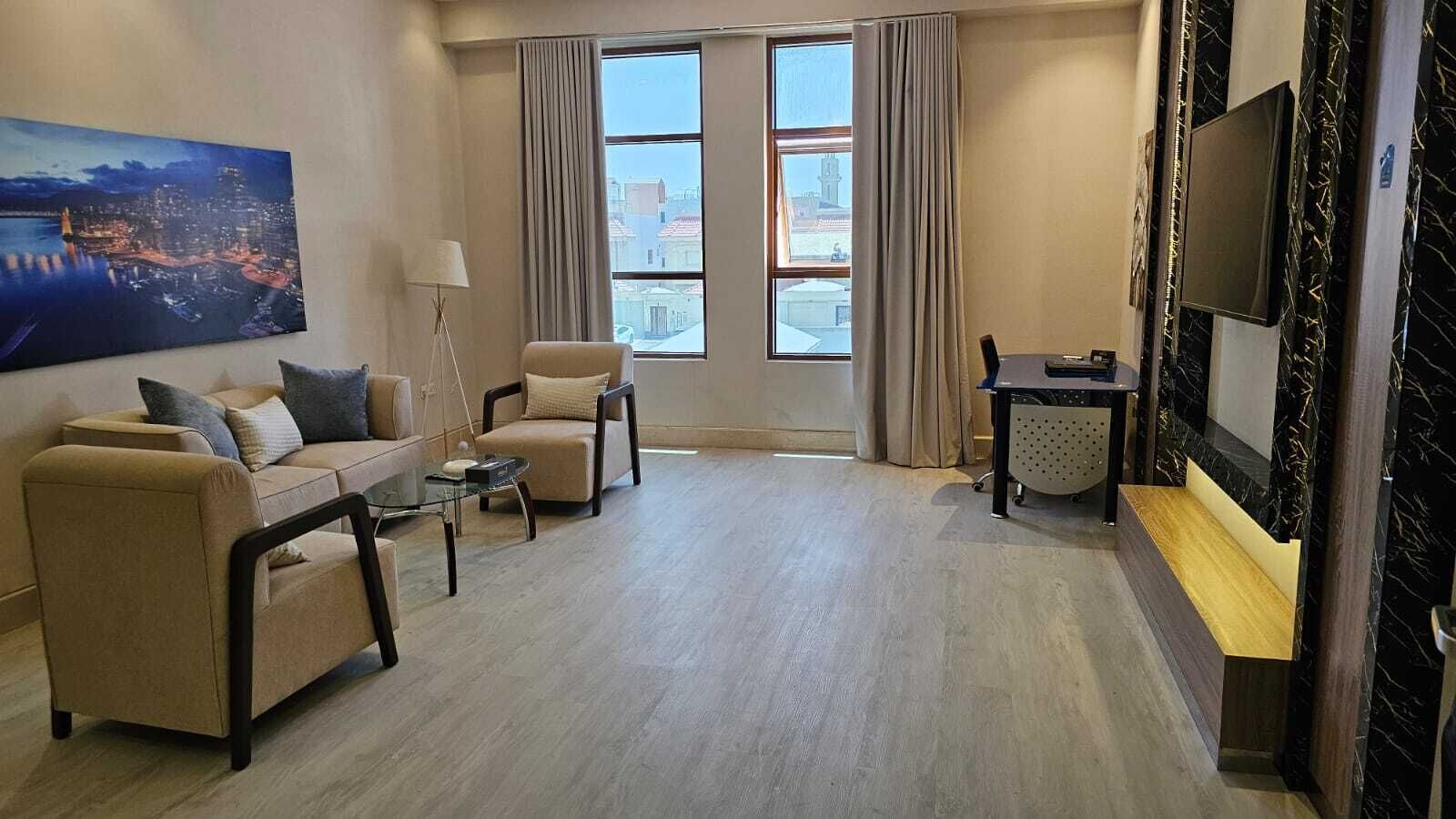 Ett modernt vardagsrum med en soffa, fåtöljer, ett soffbord, en tv och ett stort fönster med gardiner.