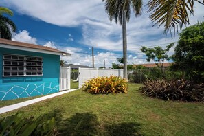 A residential property with a blue house, a fenced yard, and various plants. - Cozy 1-bedroom apartment  with King or Twin Beds (Blue Hill Rd. South)