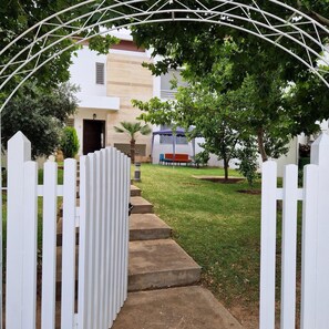 A gated entrance with a white picket fence, a concrete pathway leading to a building with a door, and a small tree in the foreground. - Villa joudia Royal golf Fès (Fès)
